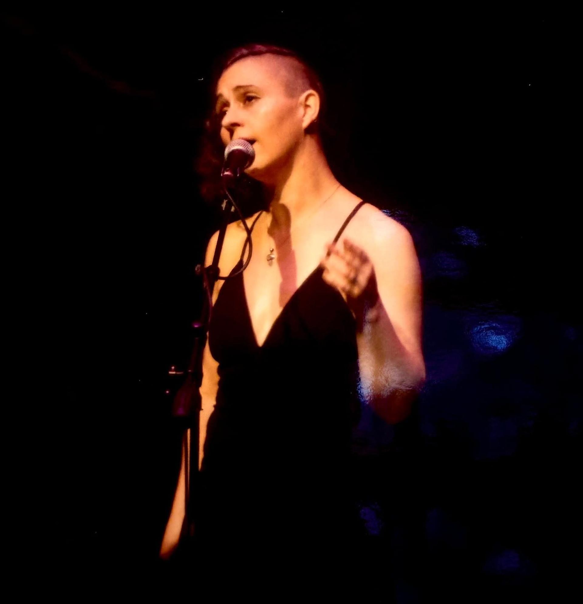 Singer in a black dress performs at a microphone under warm stage lighting.
