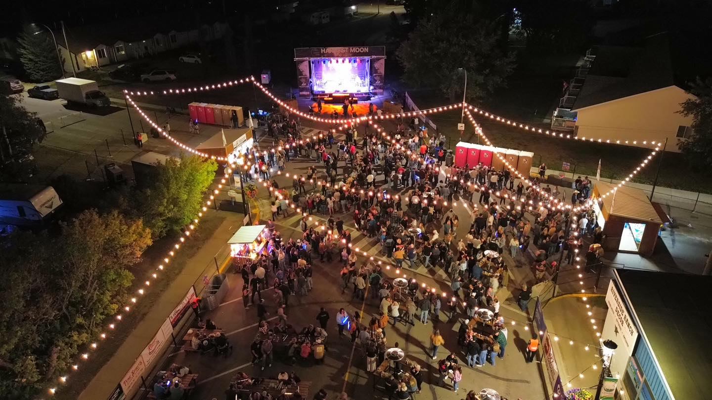 Aerial view of the Harvest Moon Festival at night with string lights, stage, vendors, and crowd.