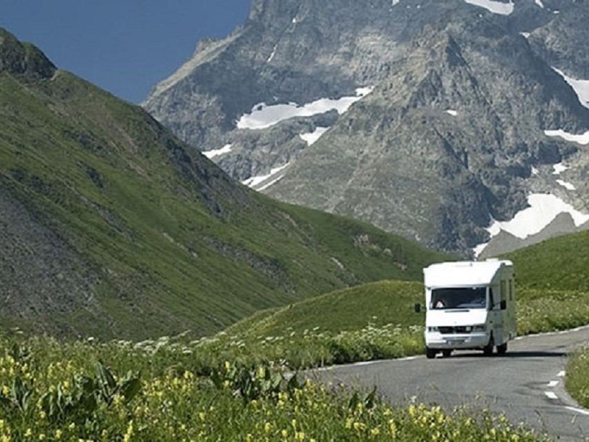 Motorhome driving along a winding mountain road with snowcapped peaks in the background.