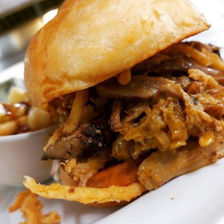 Pulled meat sandwich with saucy filling and a soft bun on a white plate.