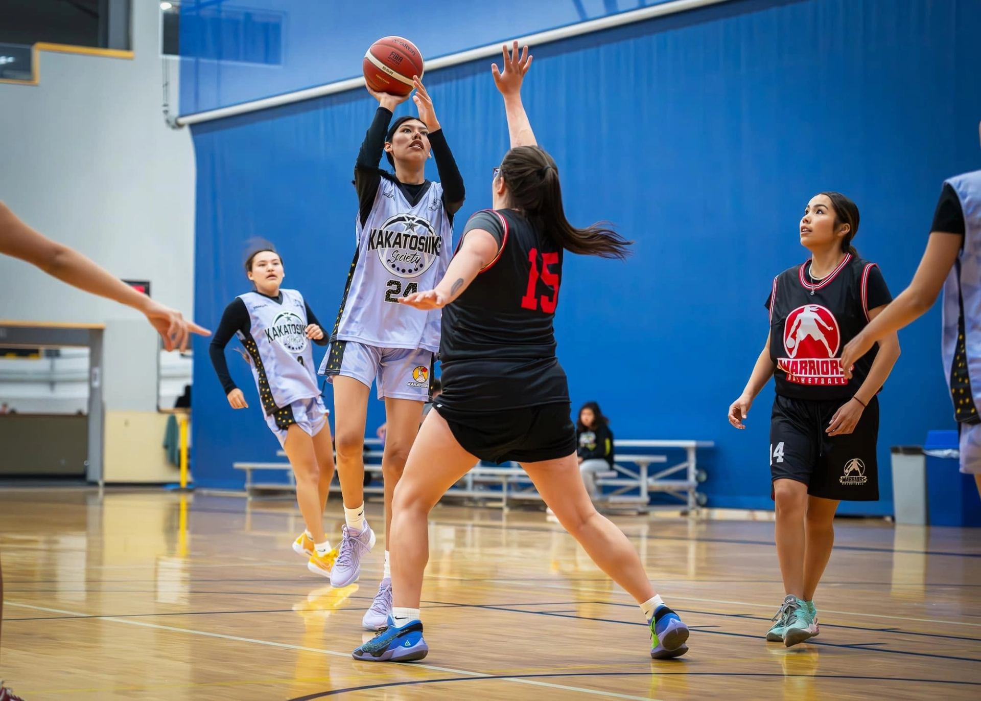 Basketball player in Kakatosiik jersey shoots over defender in Warriors jersey.