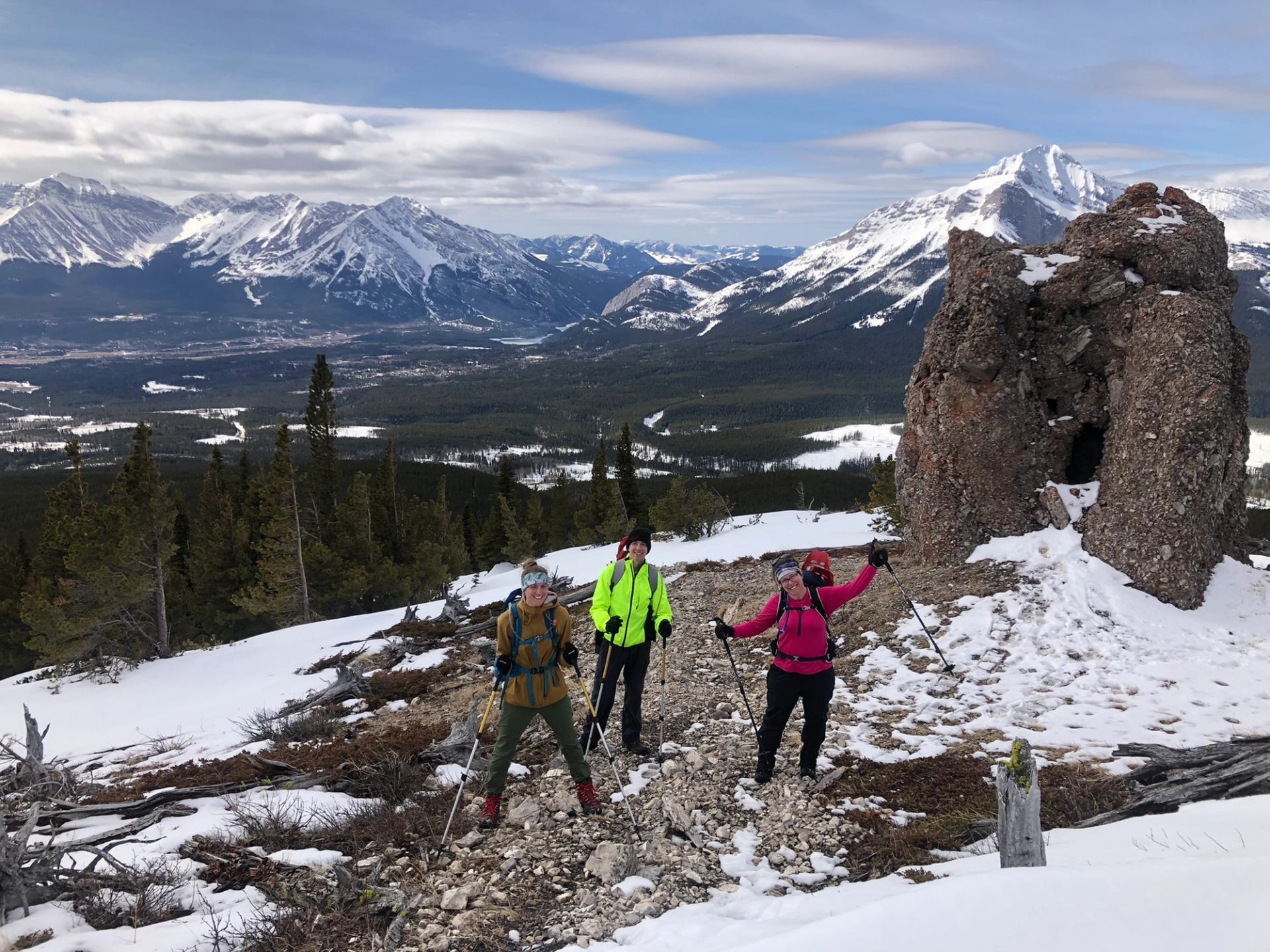 Hikers on a snowy mountain trail with rocky formations and scenic peaks in the background.
