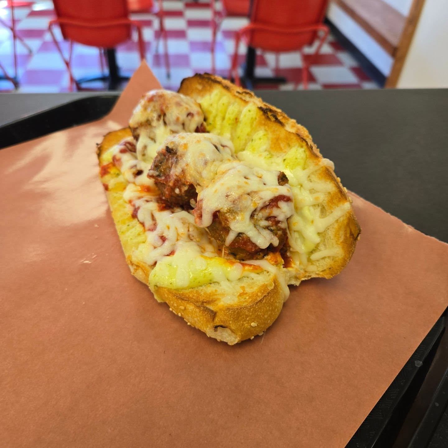 A mouthwatering meatball sandwich with Pork and Beef meatballs, tomato sauce, basil mayo, mozzarella, parmesan, garlic butter and their house made hoagie rolls.