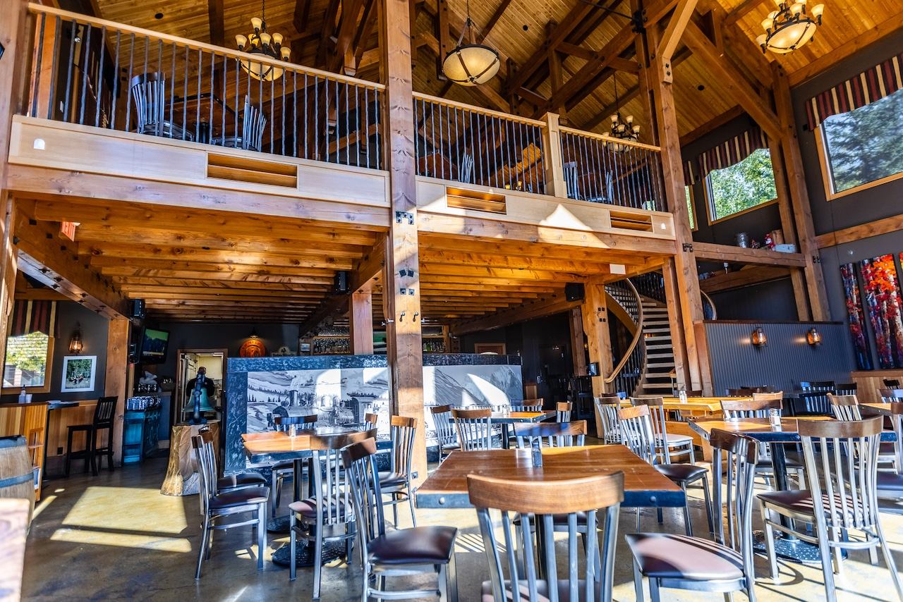 Large dining hall with tall wooden beams, loft seating, and natural light from multiple windows.