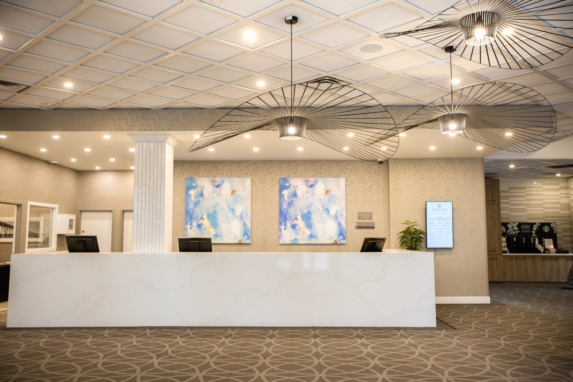 Hotel reception desk with abstract blue artwork, modern light fixtures and digital information screen.