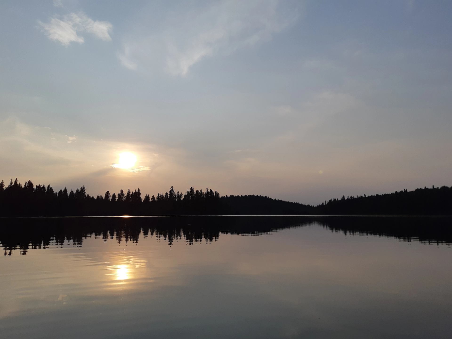Sunset over calm lake with tree silhouettes and glowing sky.