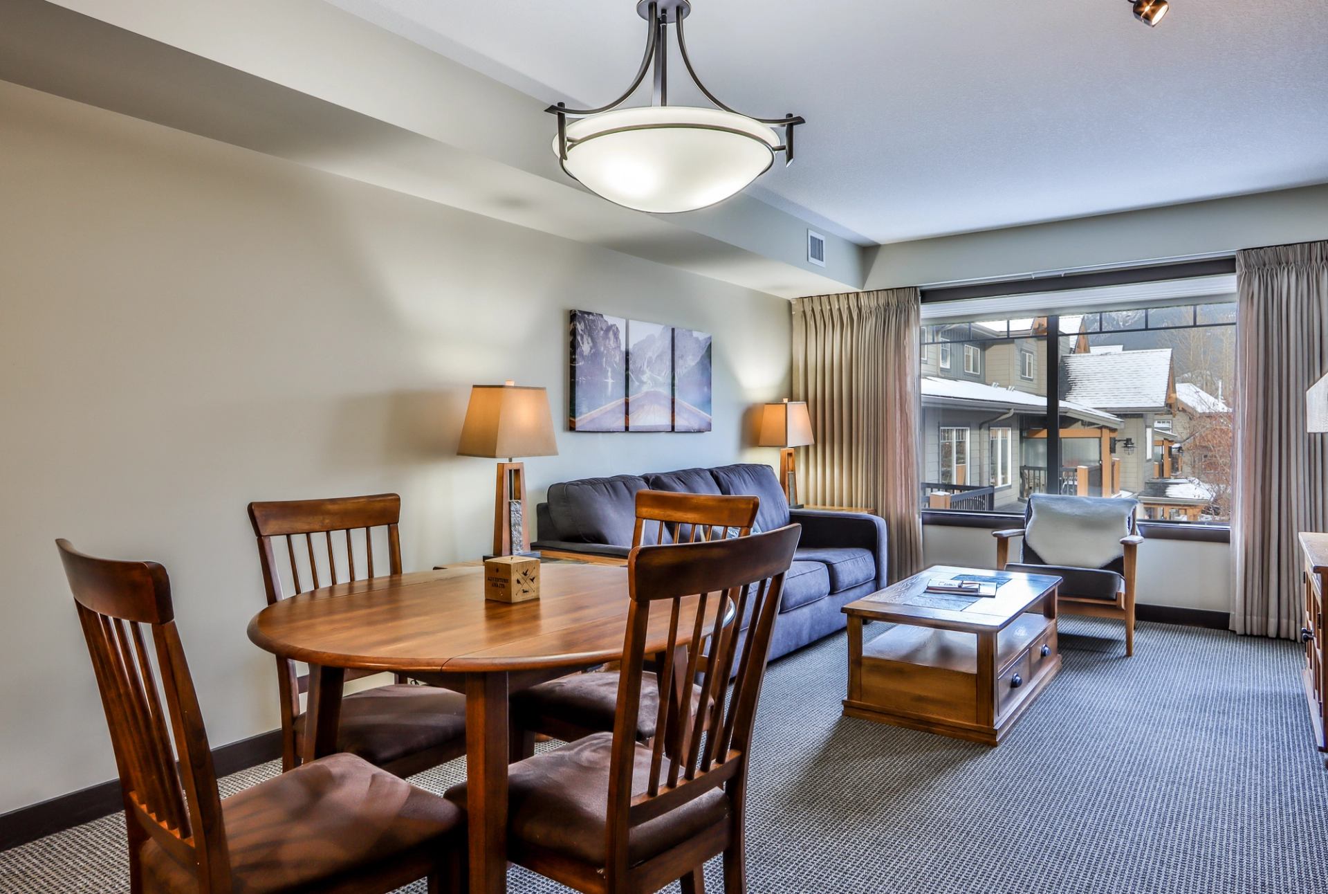 A living and dining room with a round wooden table and four chairs, a dark sofa, coffee table, and an armchair.