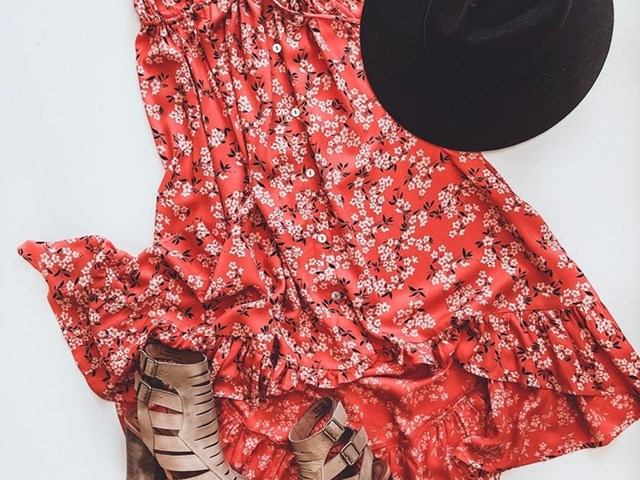 Red floral dress with white patterns, black hat, and grey strapped shoes on white background.
