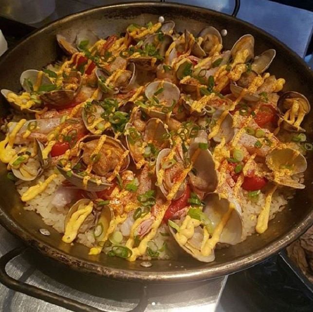 Seafood dish with clams, rice, peppers, and herbs in a pan.