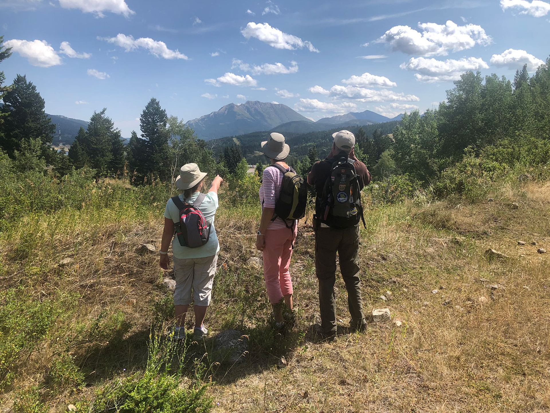 Three hikers looking toward distant mountains under blue skies.