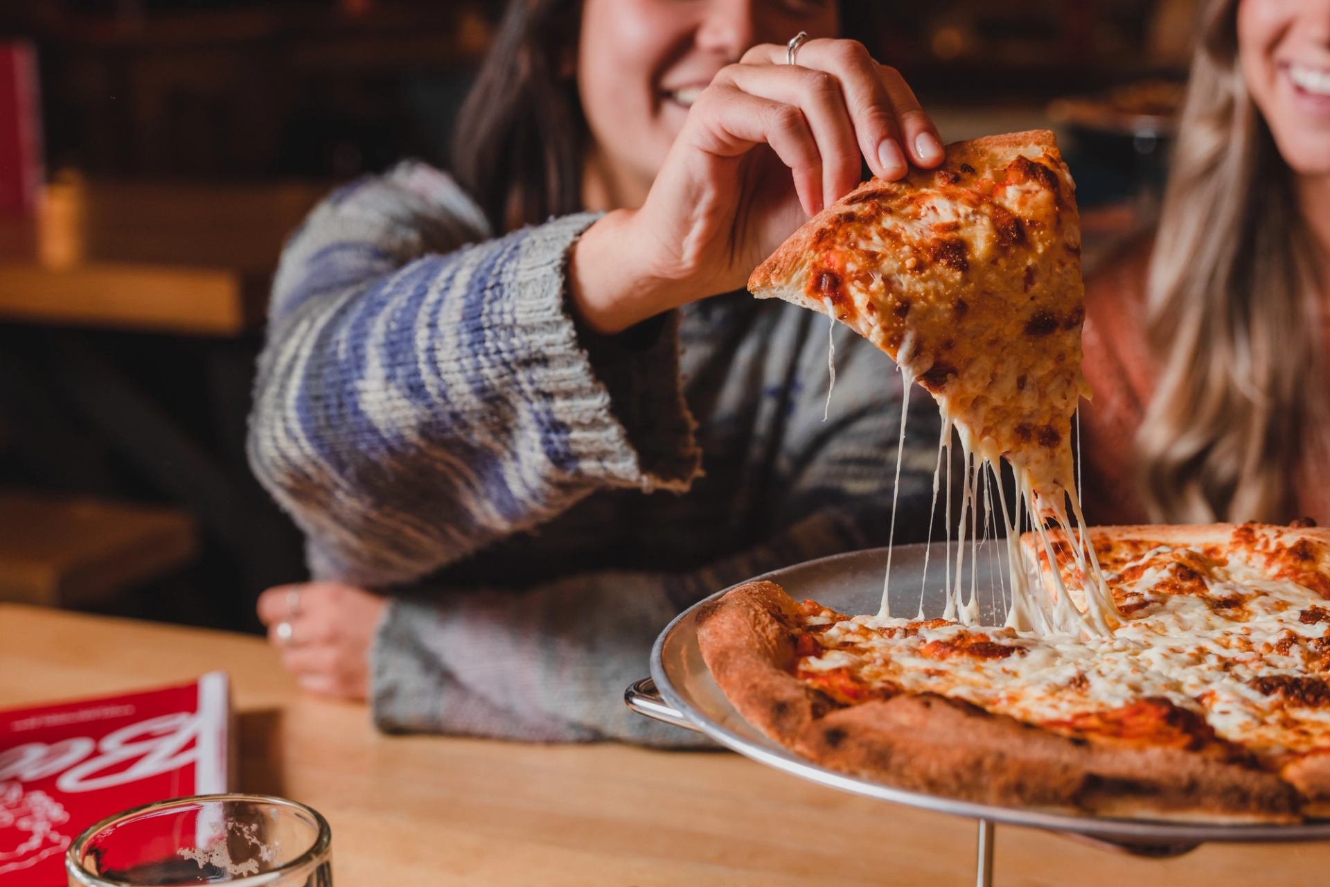 Two people sharing a cheesy pizza, with a slice being pulled and melted cheese stretching.