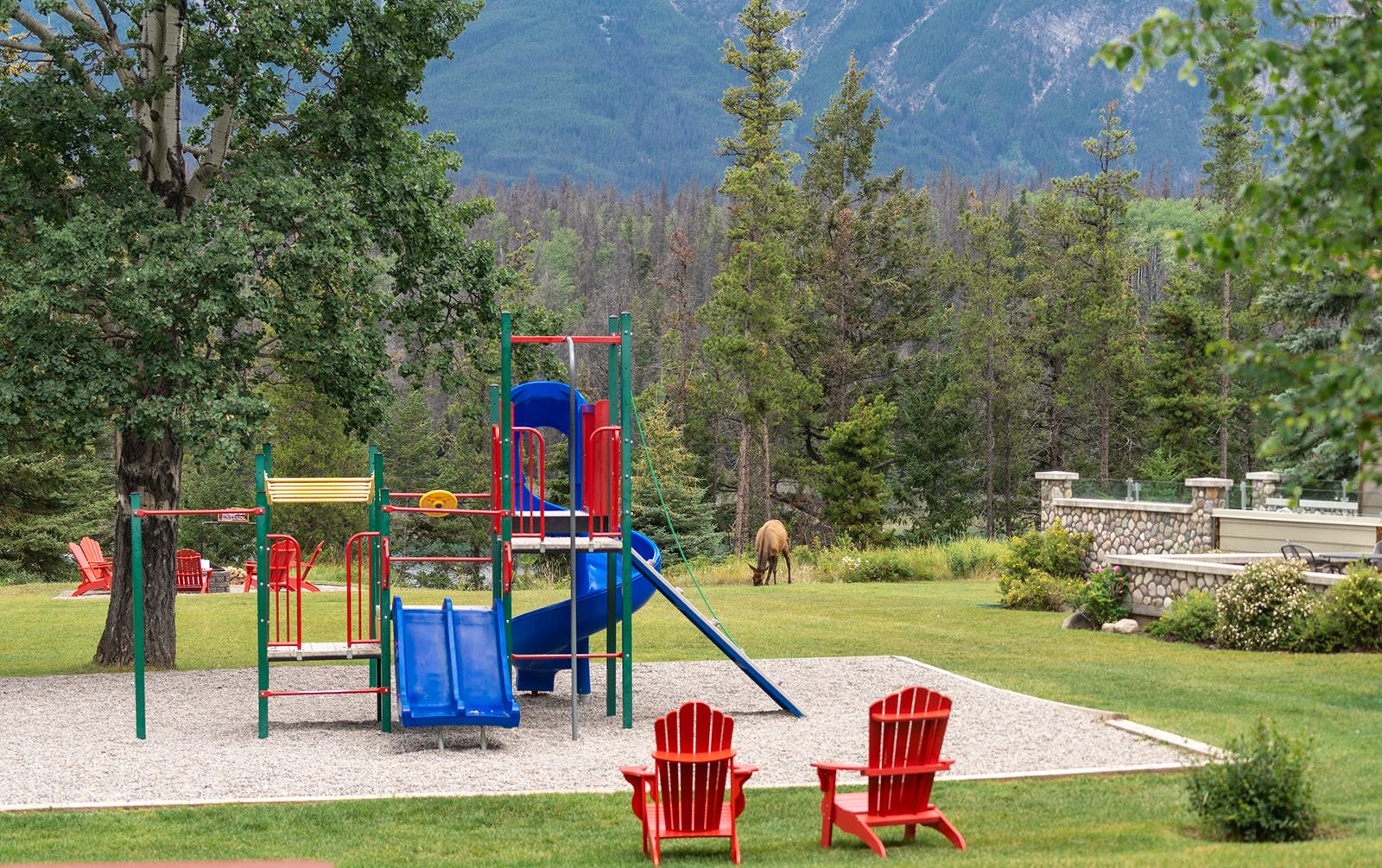 Colorful playground with chairs, trees, and mountain backdrop.