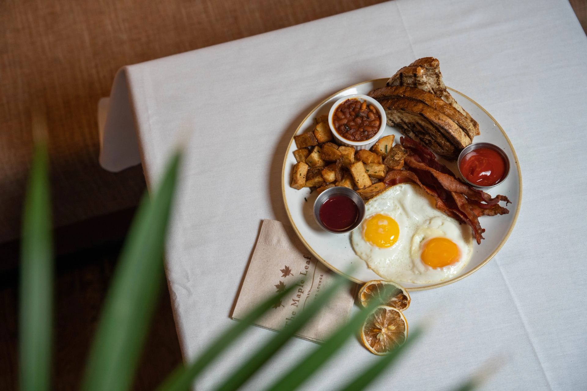 Plated sunny side up eggs, bacon, toast, hashbrowns, and brown beans.
