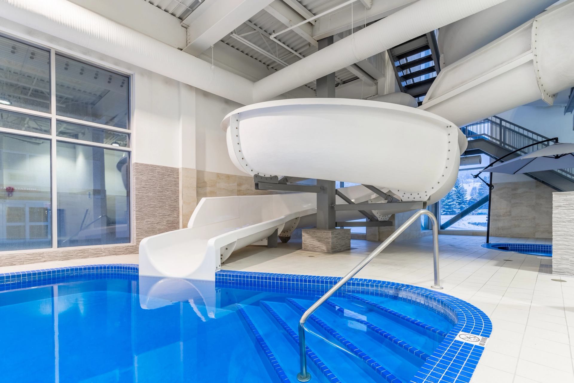 Indoor pool with blue tiles and a large white water slide in the hotel.
