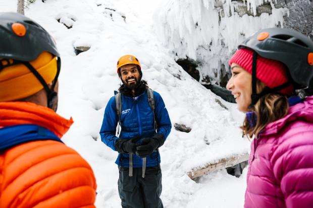 A close-up of a guide talking to two visiors with a frozen waterwall in the background.