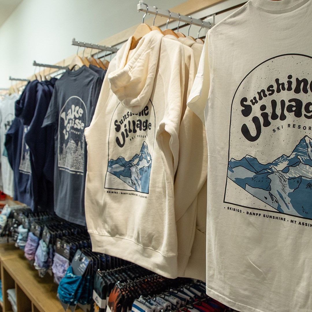 Clothing rack with Sunshine Village shirts and hoodies in various colors.