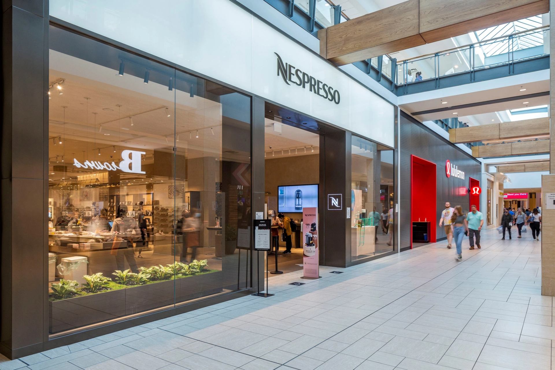 Mall corridor with Nespresso storefront and lululemon sign as shoppers walk past.