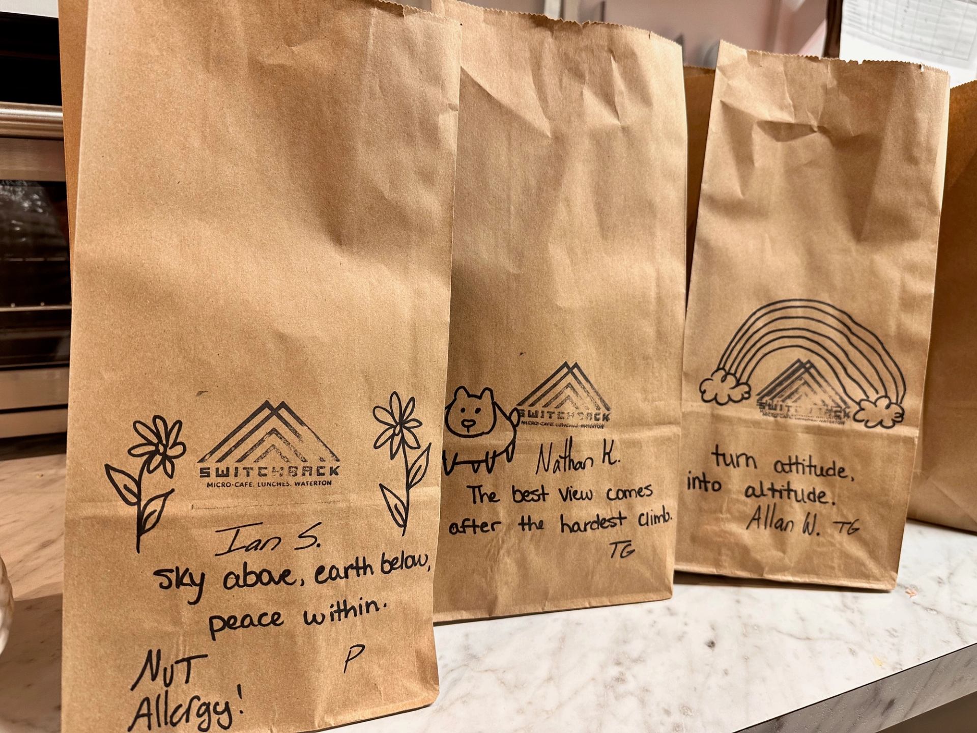 Brown Switchback Micro‑Cafe paper bags with handwritten notes lined up on a café counter.