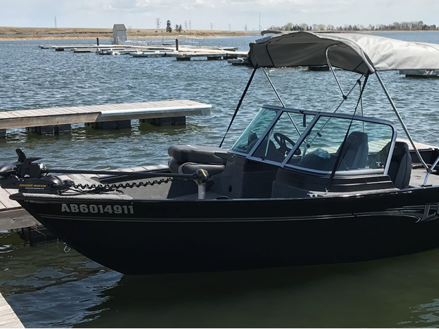 Black motorboat docked at marina with canopy and nearby boats.