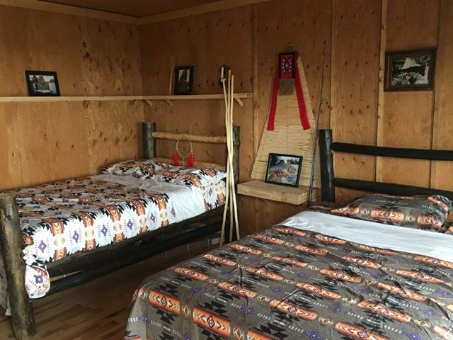 A rustic wooden room with two beds featuring Native American-style blankets. Walls adorned with photos and traditional decor create a cozy, cultural ambiance.