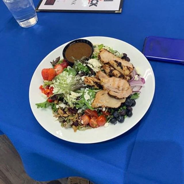 Plate of salad with grilled chicken, berries and dressing on blue tablecloth.