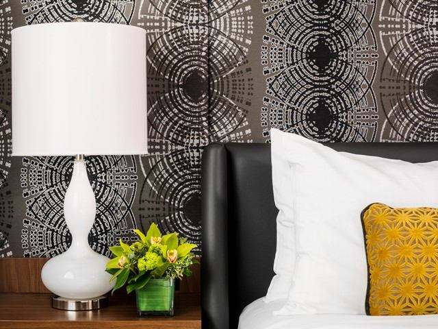Room detail with lamp, floral decor, patterned wallpaper, and orange accent pillow.