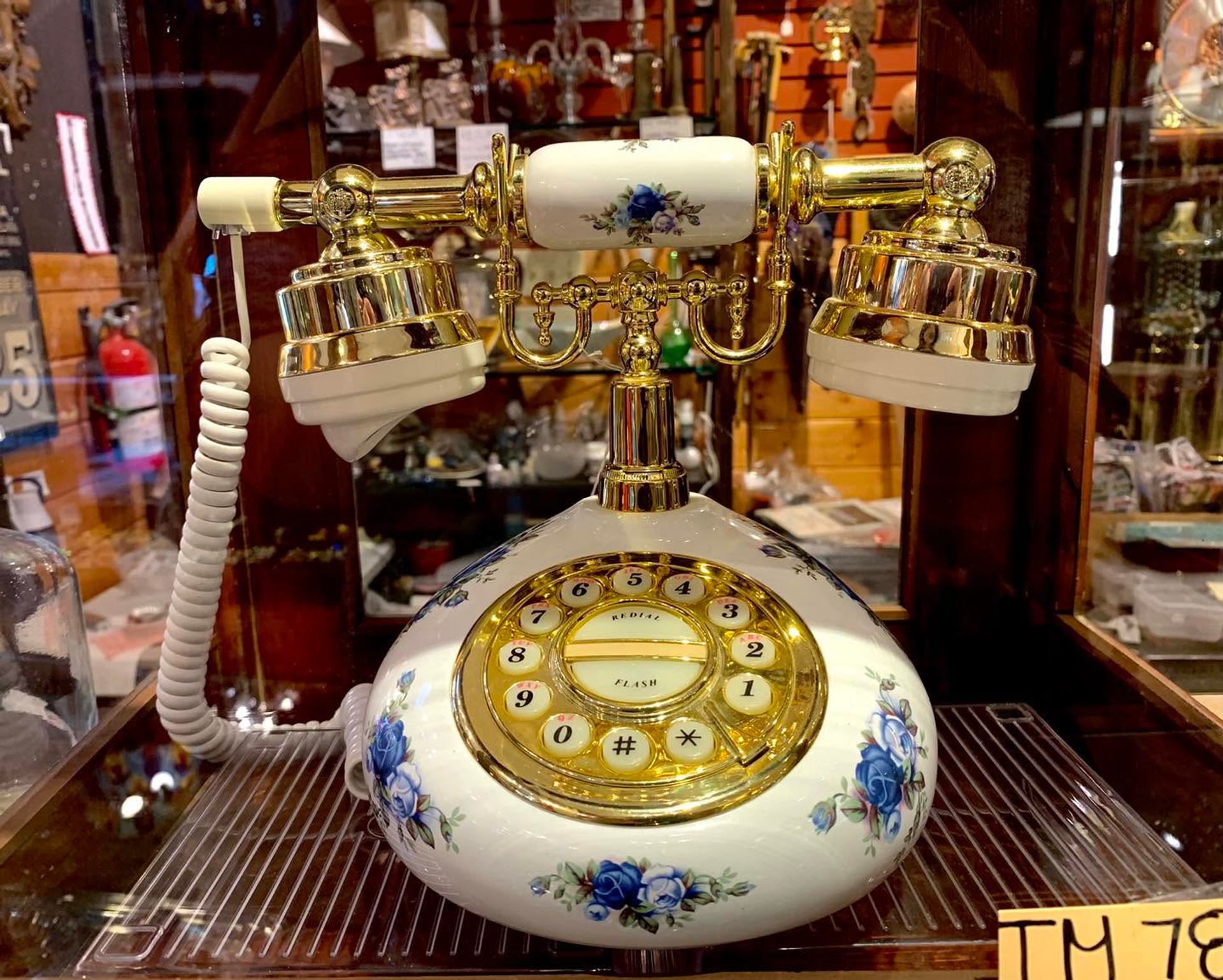 Vintage rotary telephone with gold trim and blue floral pattern on display shelf.