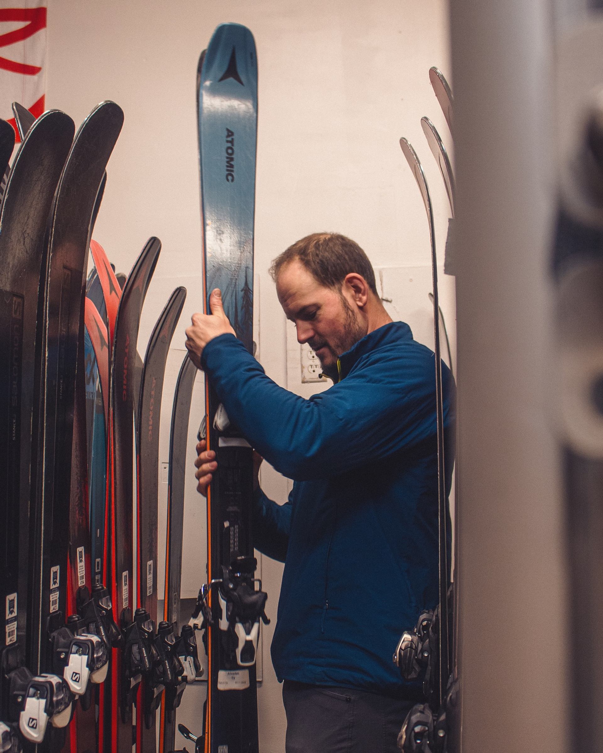 Person holding a ski among rows of skis in a rental shop