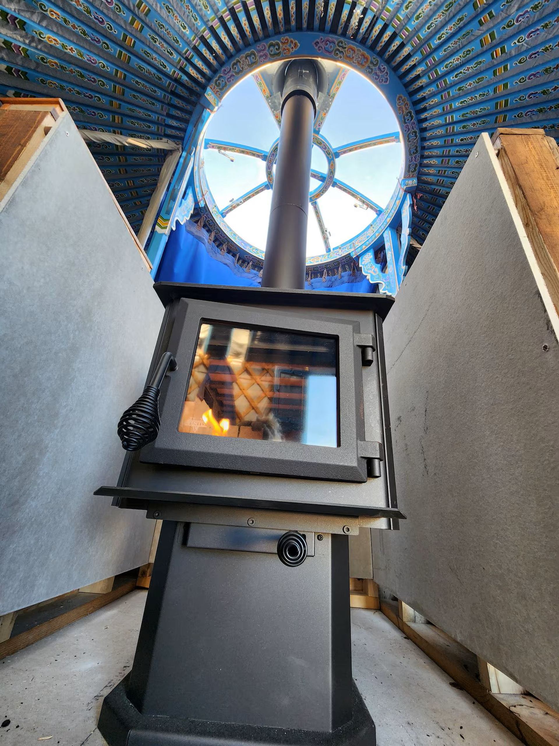 Wood stove inside yurt beneath a round skylight with painted beams.