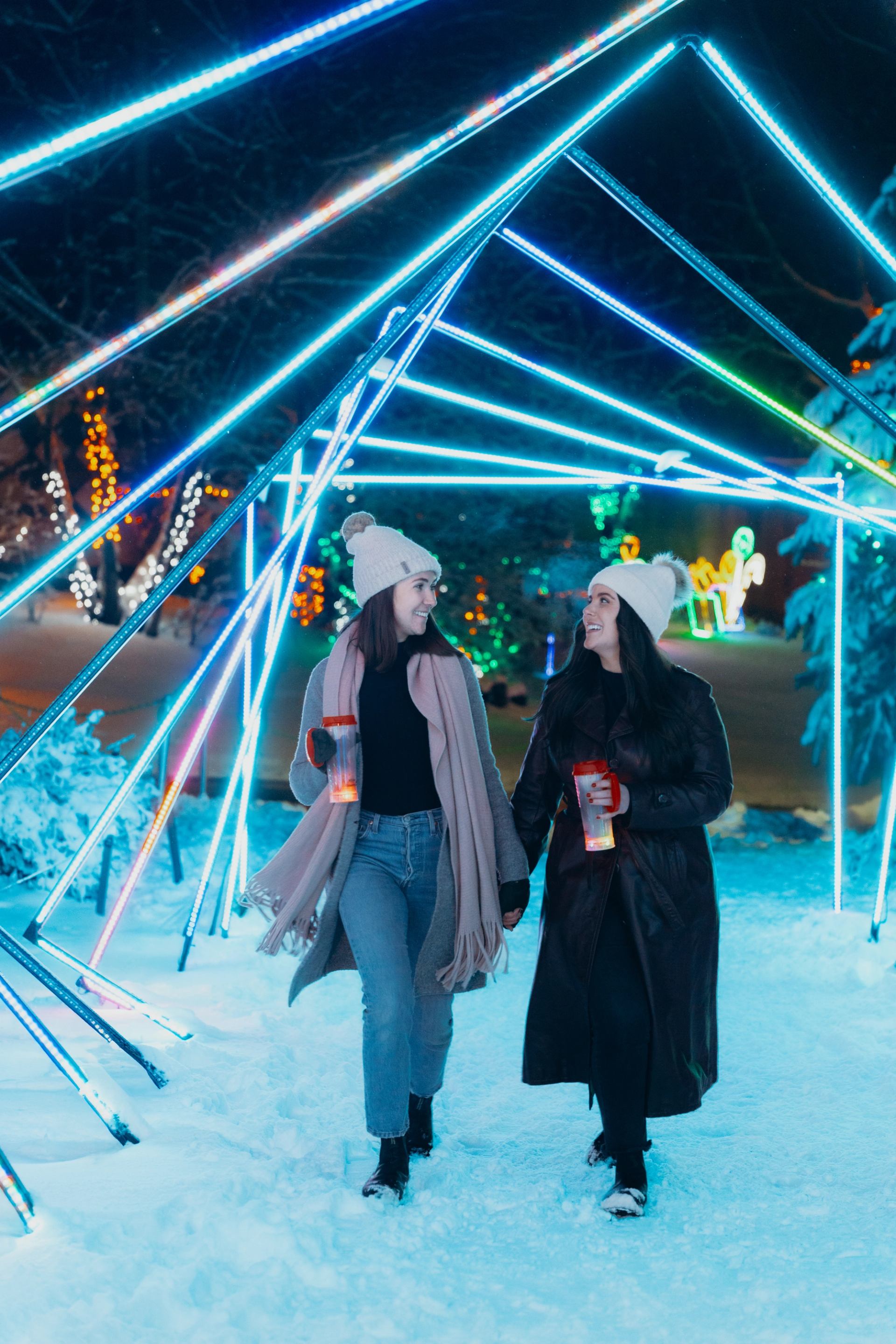 Two people walking through a snowy tunnel of glowing blue and white lights.