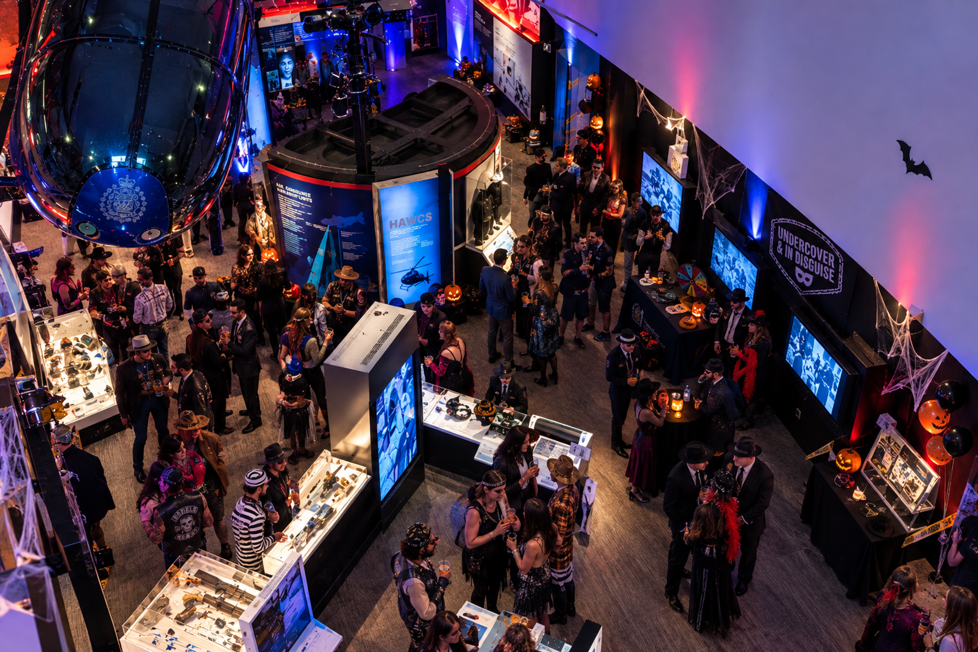 Costumed guests gather among aircraft exhibits and Halloween decorations in a museum.