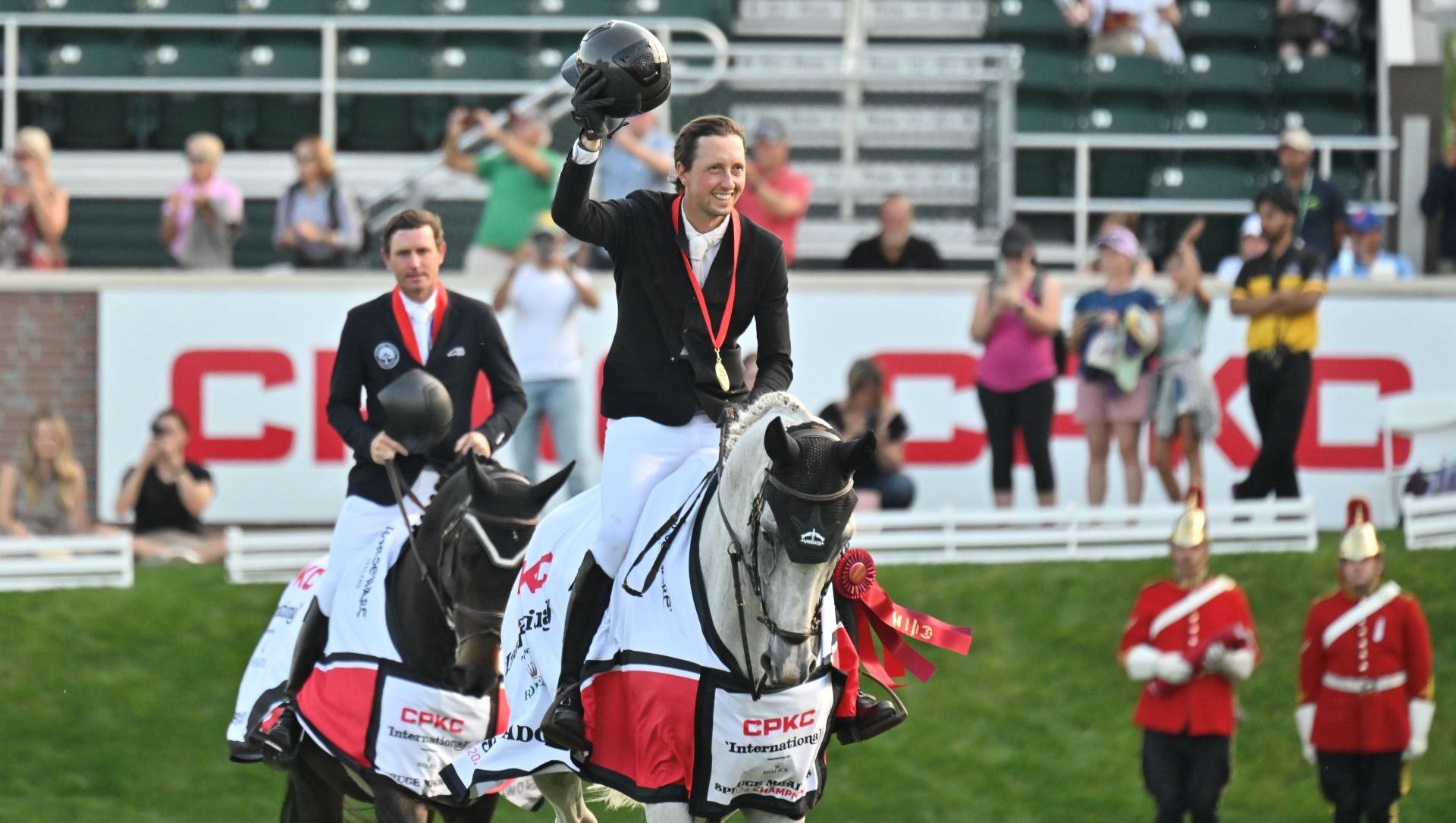 Two equestrians on horses with medals and ribbons at a competition.