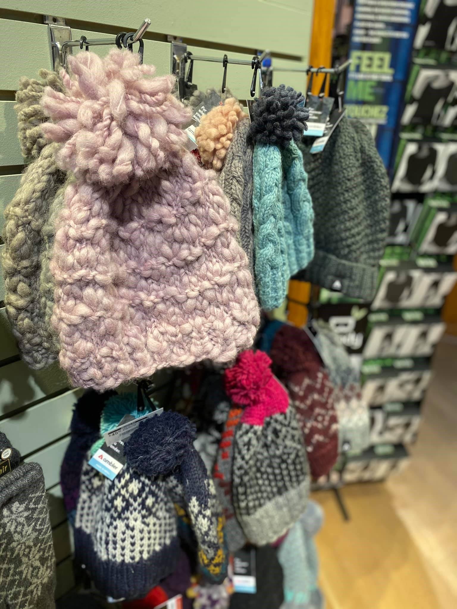 Knitted toques with pom-poms hanging on a retail display rack.