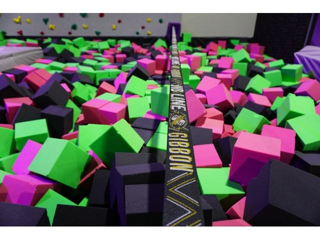 Slackline stretching over a foam pit filled with bright green, pink, and black foam cubes.