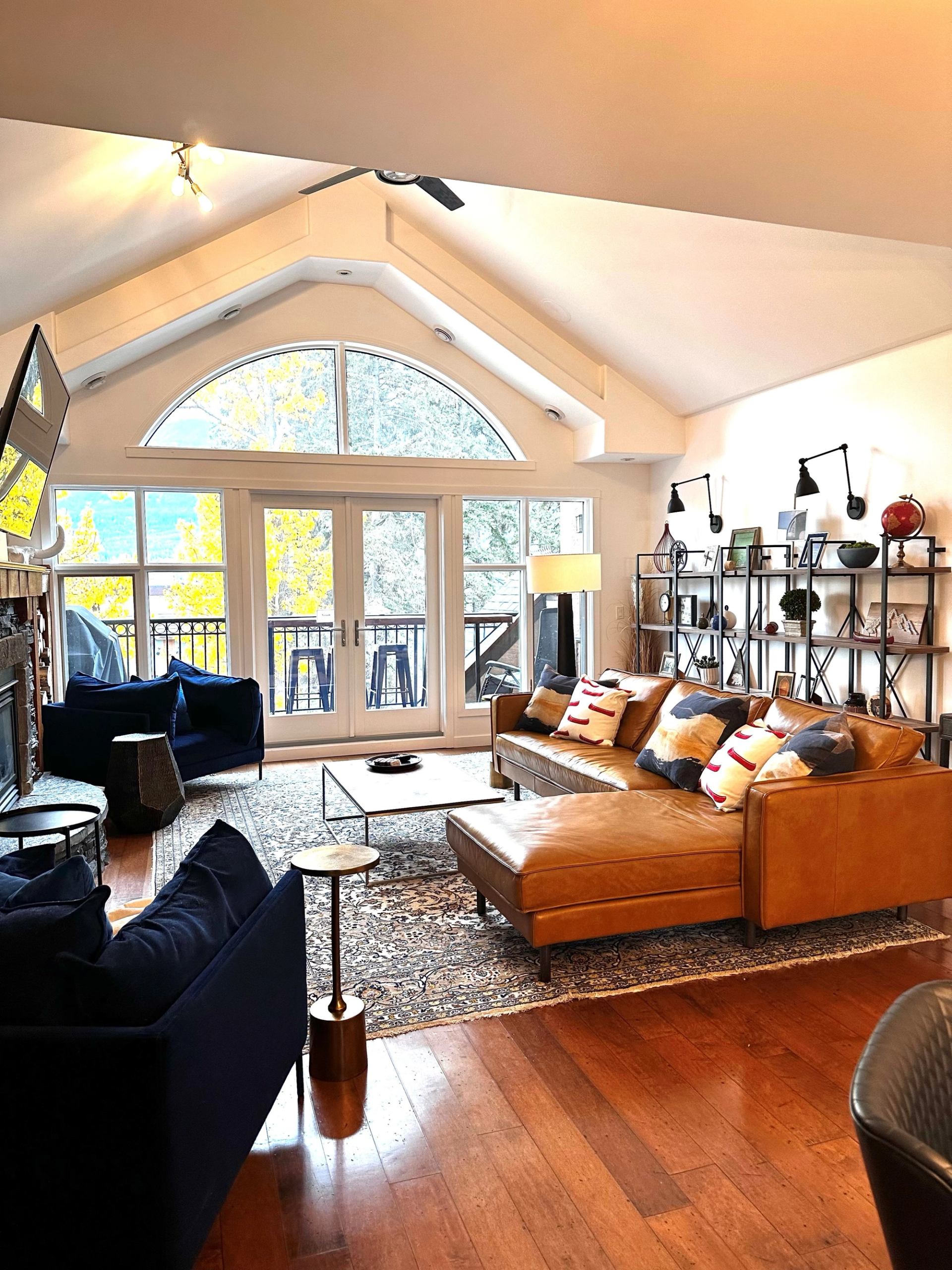 Bright living room with vaulted ceiling, leather sofa, and large windows opening to a balcony.