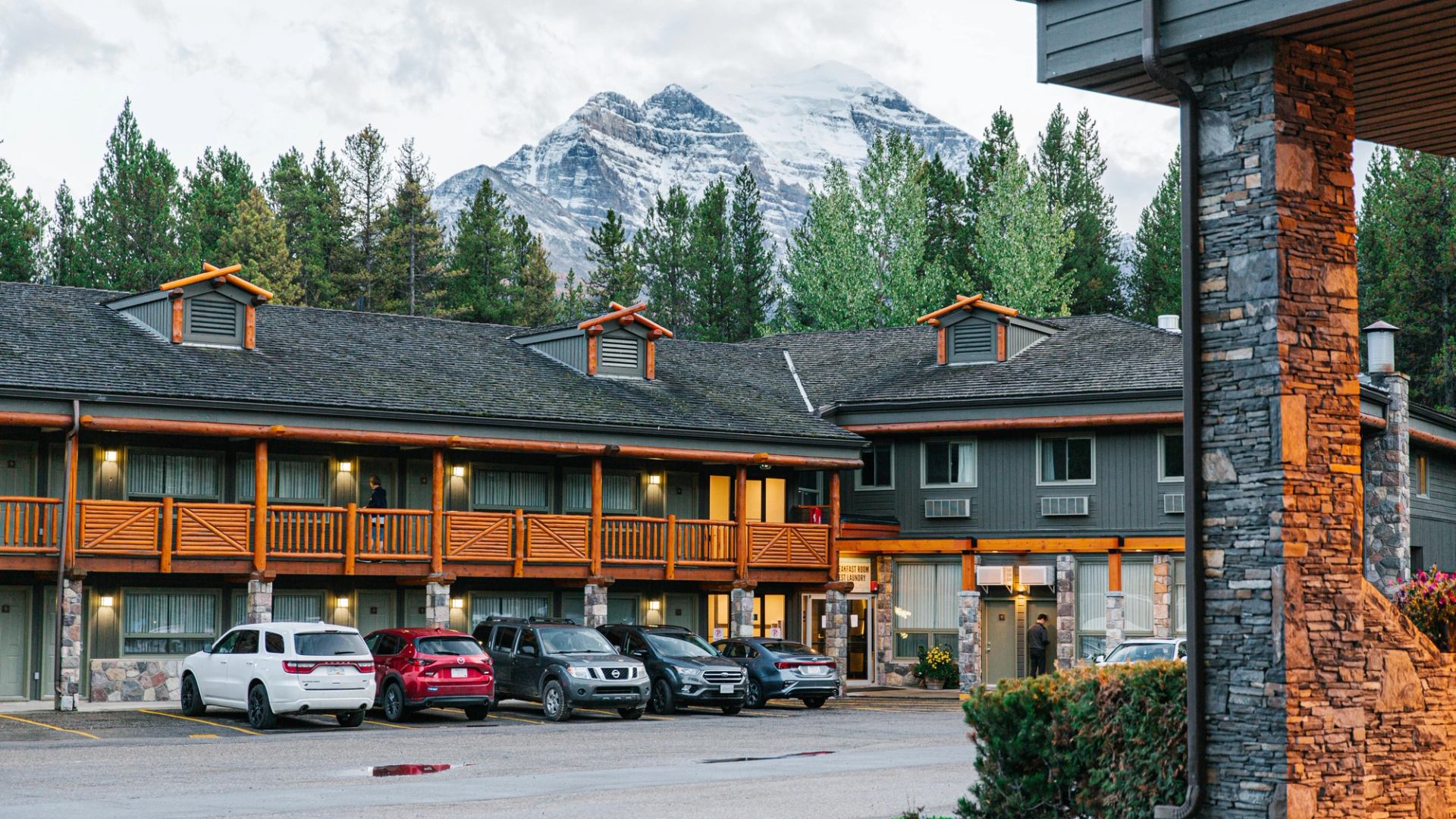 Exterior of Mountaineer Lodge with guest cars parked in front and a massive snow-capped peak behind.