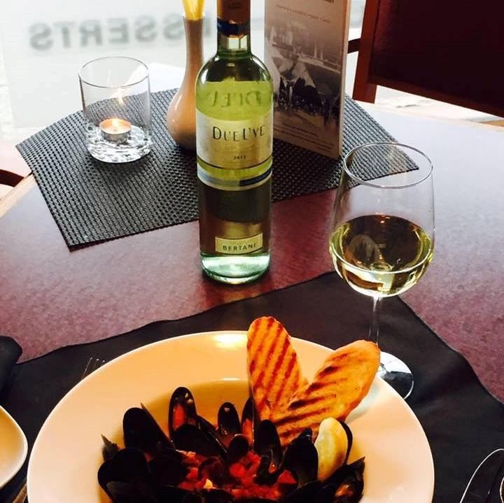 Plate of mussels in sauce with grilled bread, served alongside a glass and bottle of white wine on a table.
