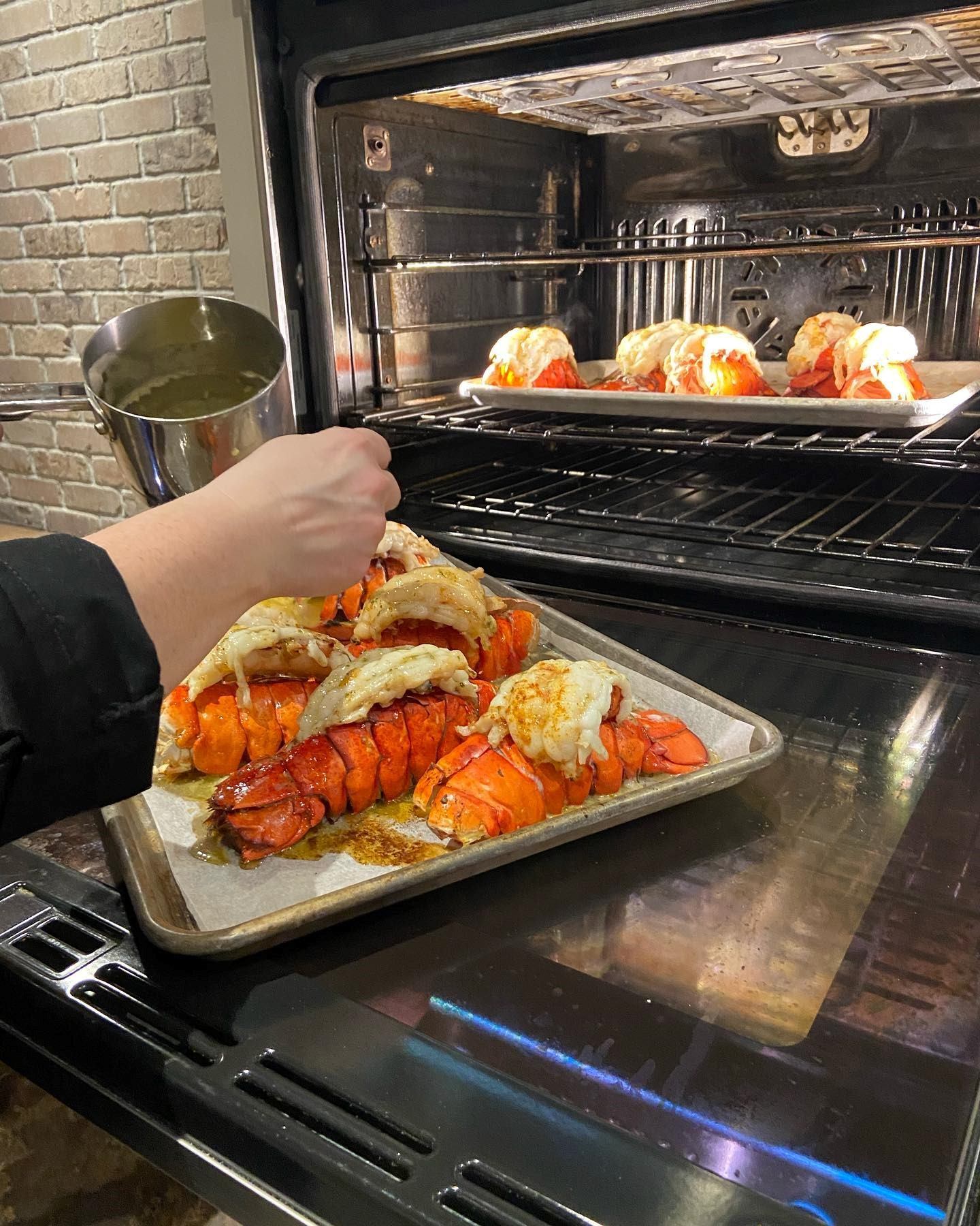 Lobster tails being basted and baked in an oven.