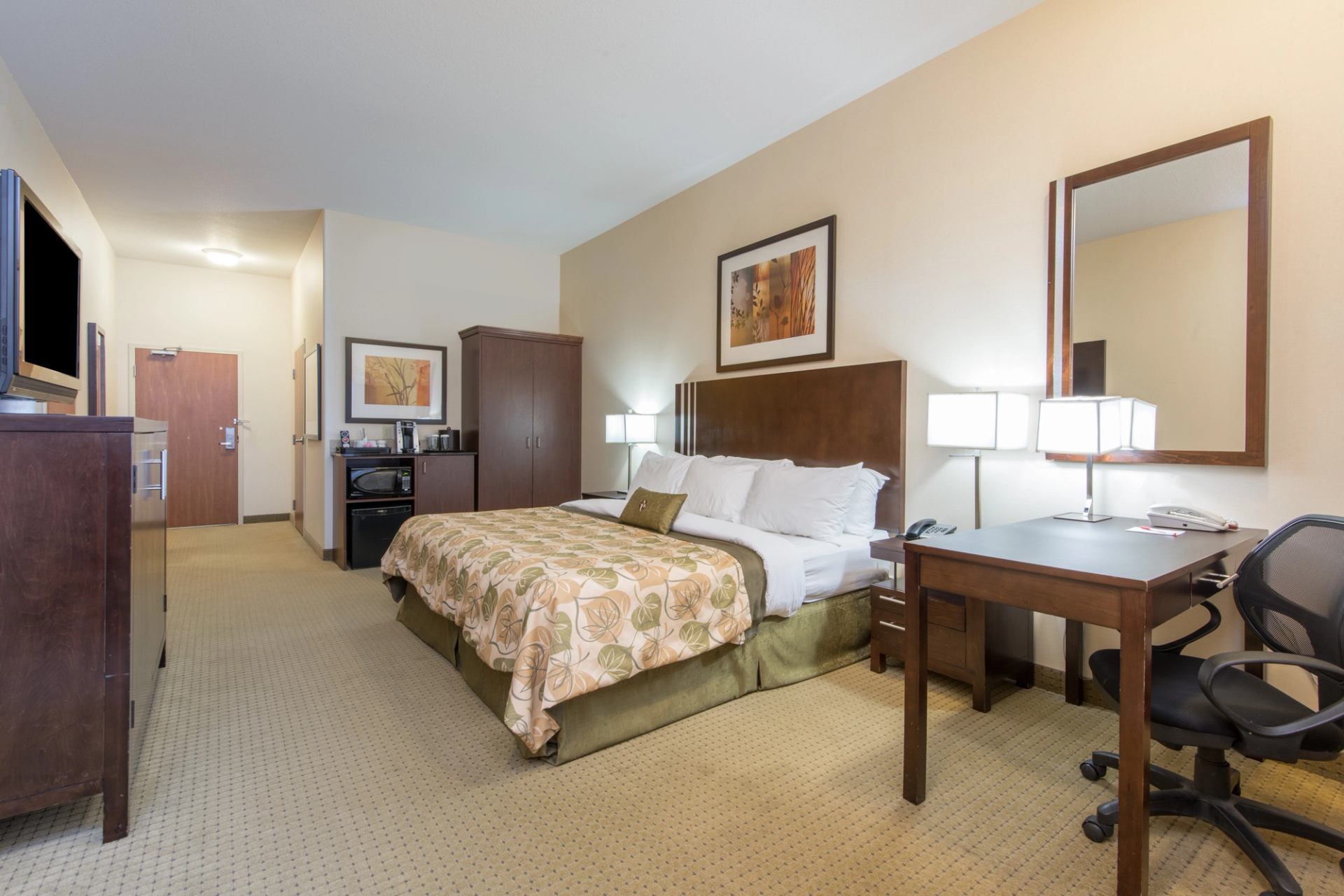 Hotel room with king bed, desk, office chair, wardrobe, and kitchenette area.