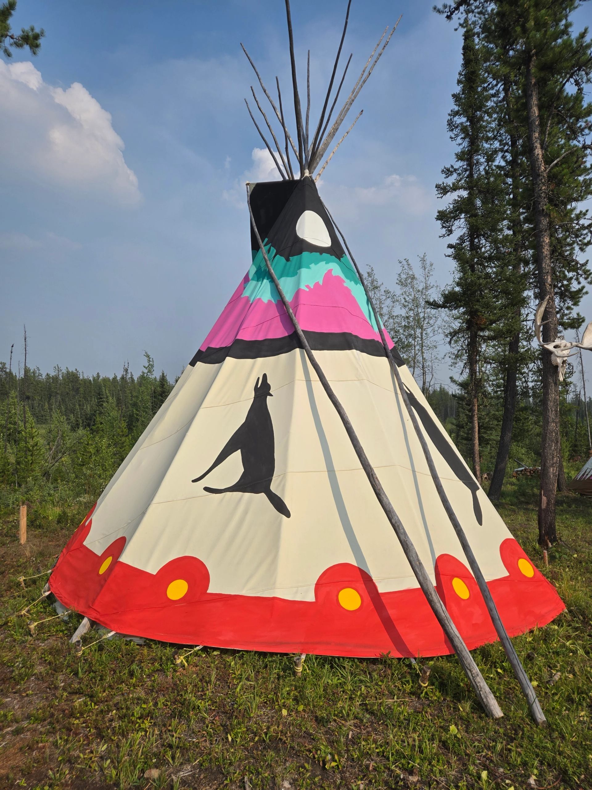 A painted teepee with Aurora and a moon on to top, howling wolfs on the middle, red, yellow  bottom