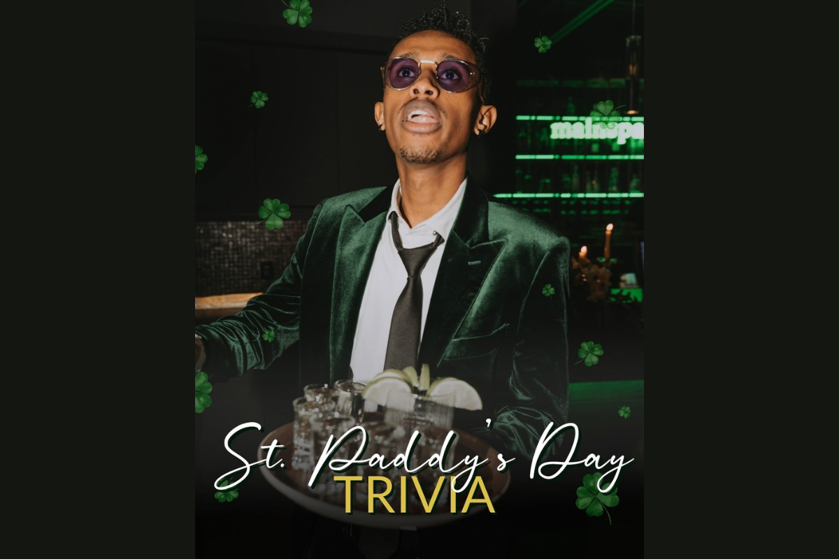 Person in a green velvet jacket stands at a bar with cocktails, surrounded by St. Patrick’s Day décor and shamrocks.