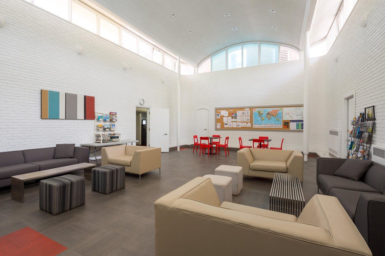 Spacious lounge with soaring curved skylight, modern sofas in grey and tan, red dining table.