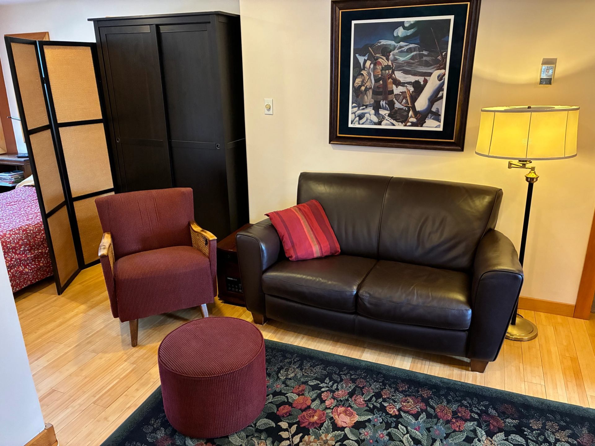 Living room with brown leather sofa, red chair, ottoman, floor lamp and artwork.