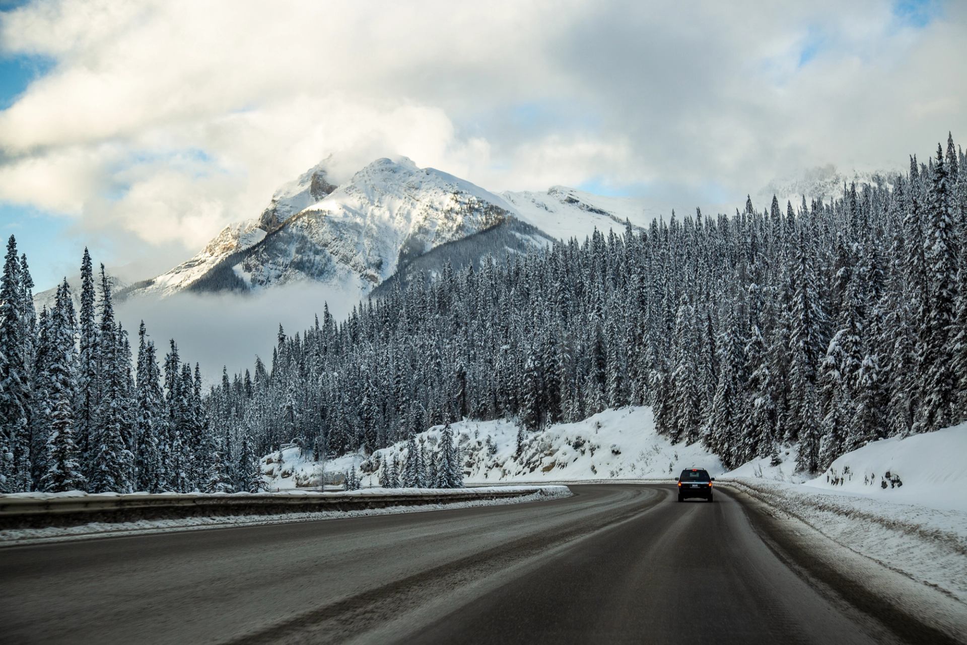 Car driving on a snowy mountain road lined with pine trees.