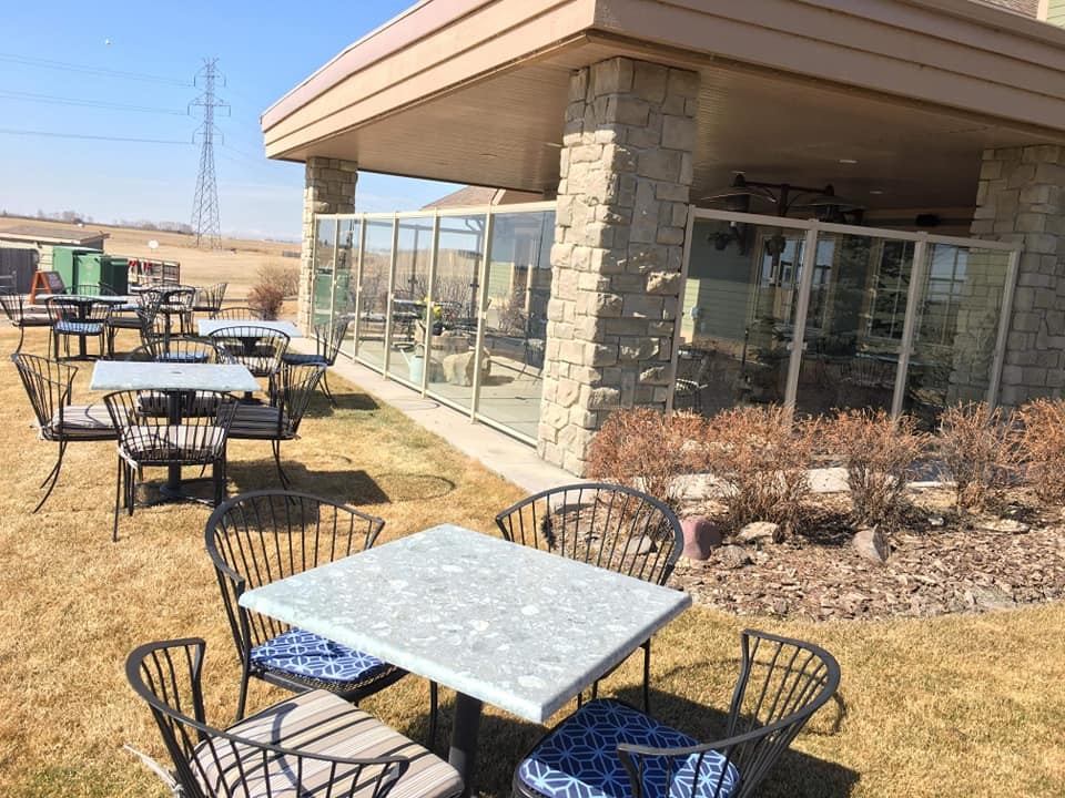 Outdoor tables and chairs on a patio beside the clubhouse with clear skies