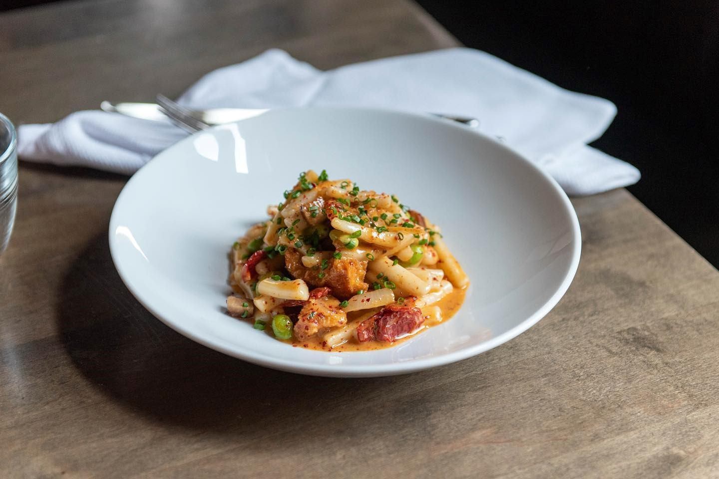 Model Milk pasta dish with vegetables and herbs in a white bowl on a wooden table.