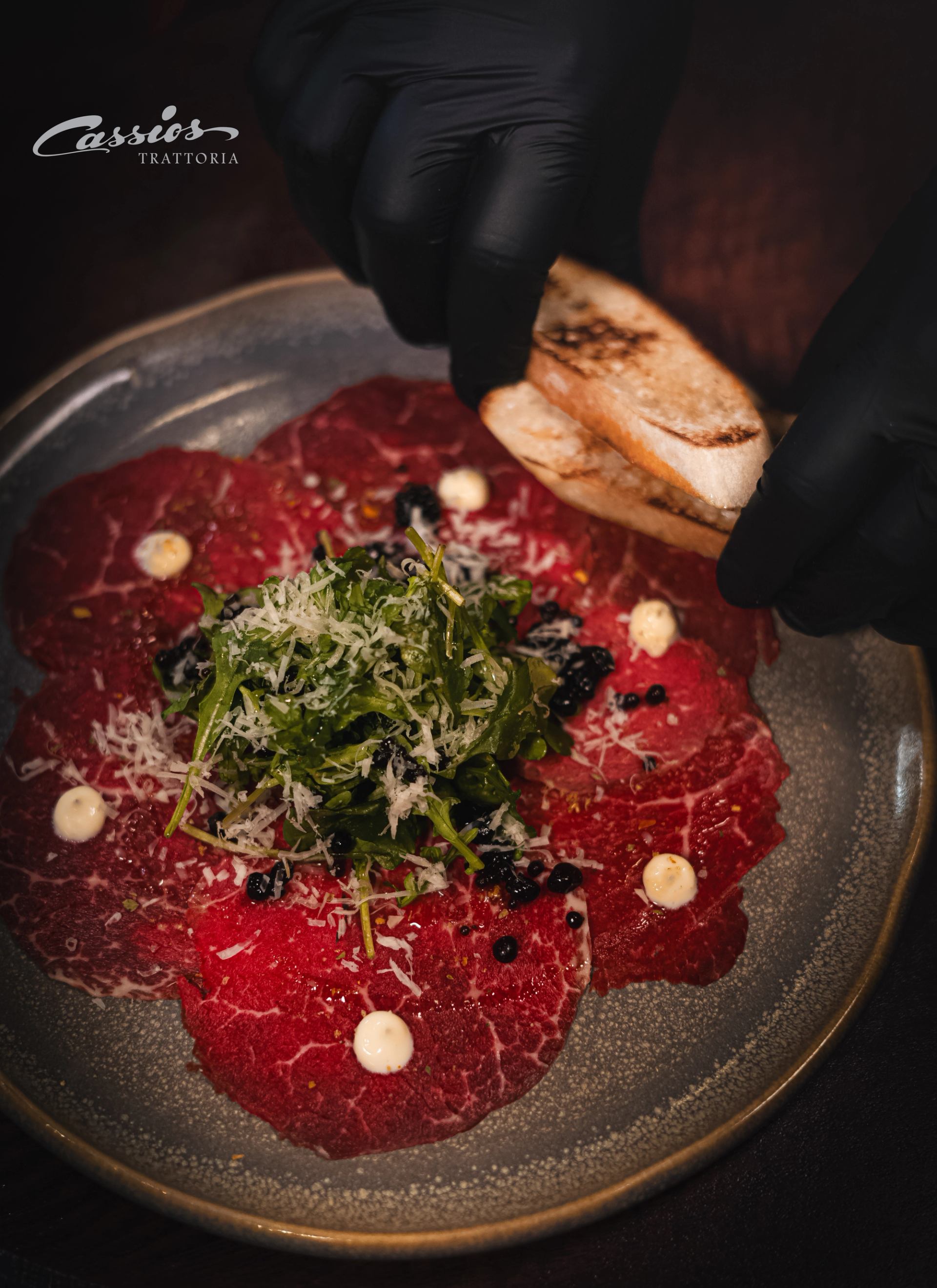 Beef carpaccio with arugula, grated cheese and crostini on a grey plate.