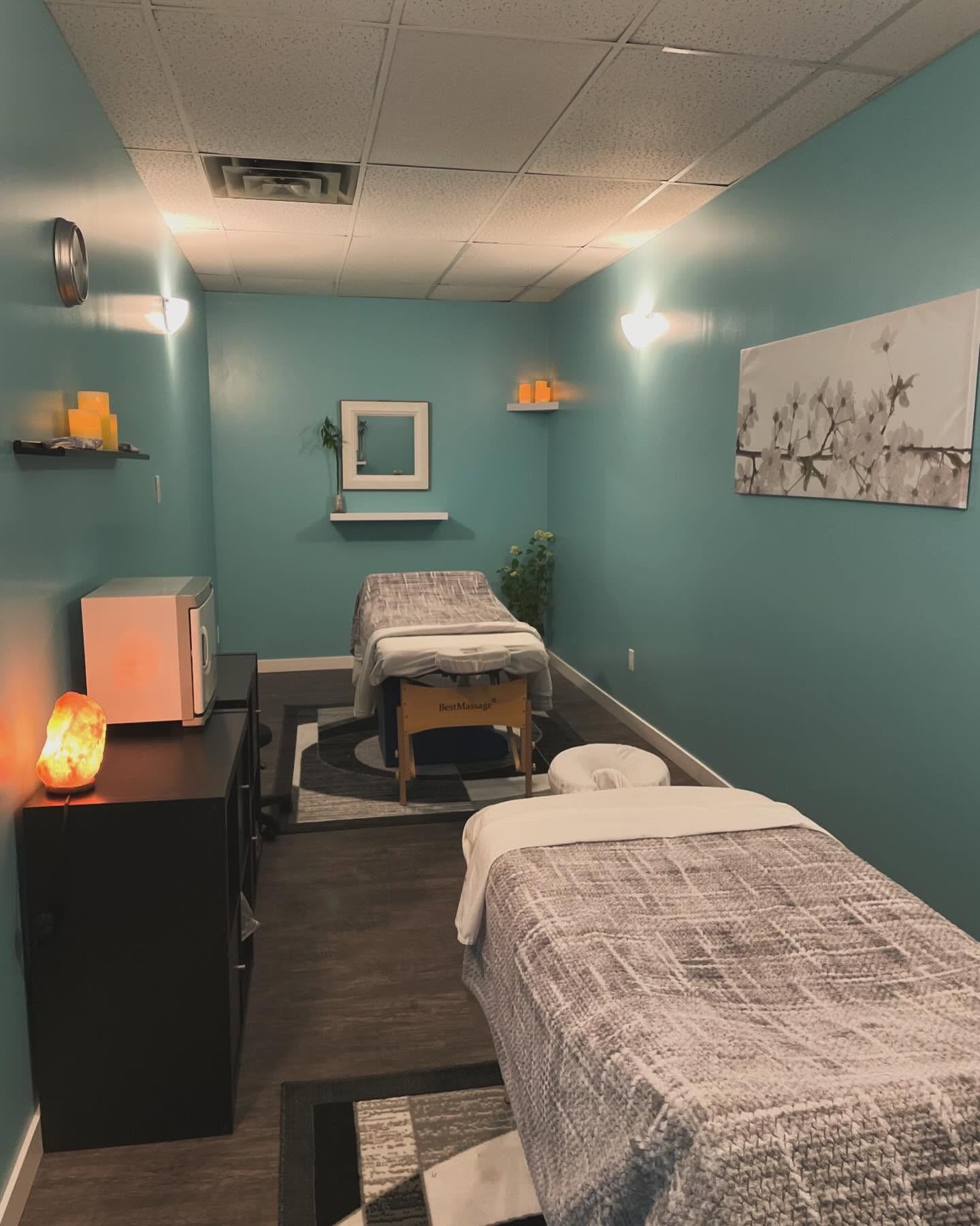Massage room with two covered tables, teal walls, candles and framed floral artwork.