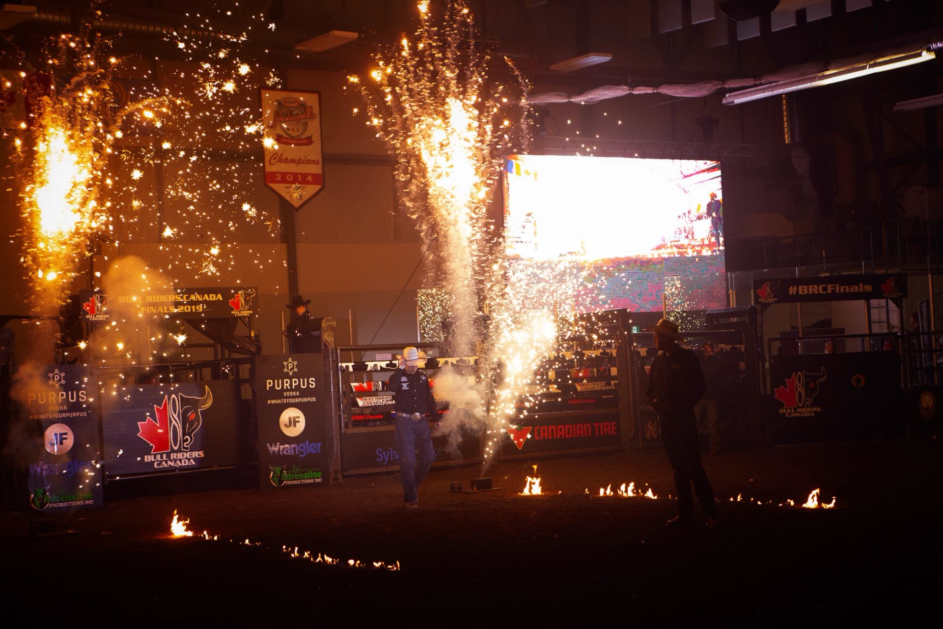 Indoor rodeo arena entrance with fireworks, flames and Bull Riders Canada signage visible.