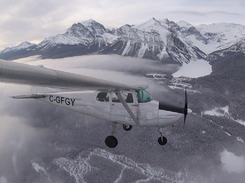 Small plane flying over snow-covered peaks and clouds near Red Deer Regional Airport.
